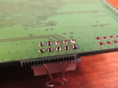 Photograph of the solder joints on the header pins.  The steadying binder clip can be seen underneath.